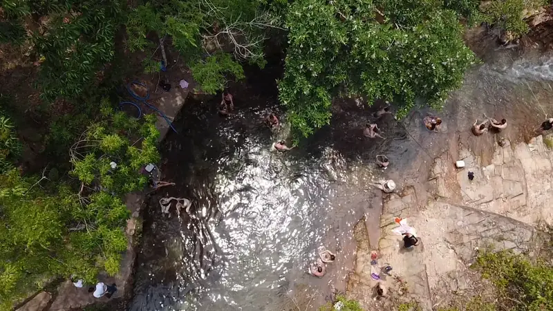 Vista do alto do rio correndo entre a mata e as pedras, com banhistas na beira